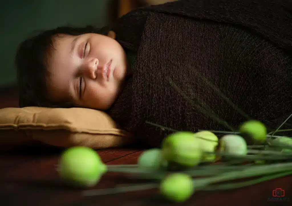 Newborn baby sleeping peacefully, wrapped in a dark blanket.